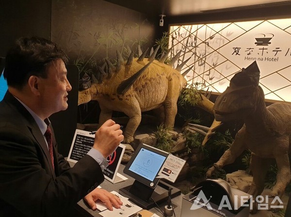 조피터성규 한국AI호텔·문화관광협의회 회장이 일본 헨나호텔 도쿄 니시카사이에서 투숙객을 맞이하는 AI 공룡호텔리어와 체크인을 하는 중이다. (사진=한국AI호텔·문화관광협의회 제공).