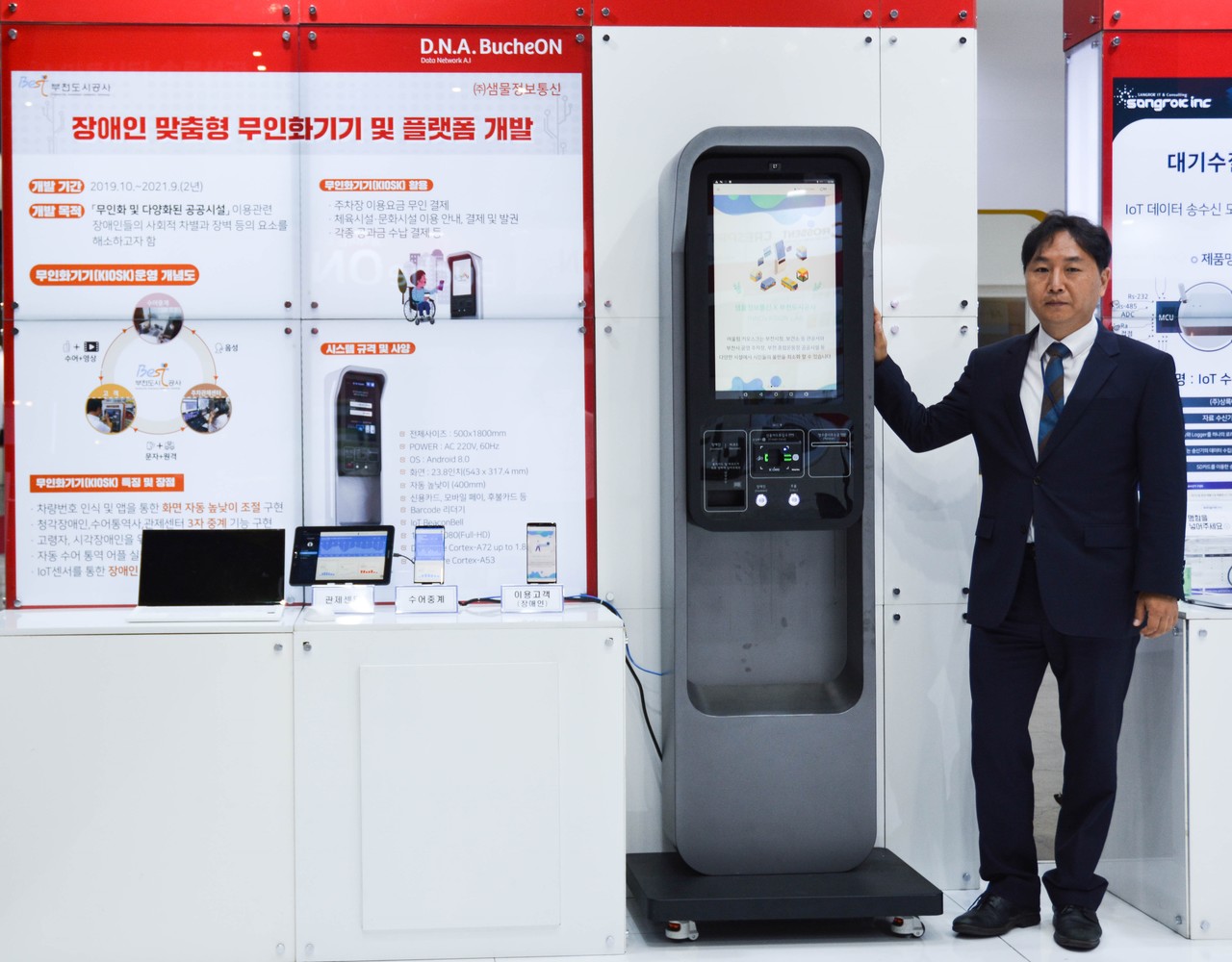 백현민 샘물정보통신 대표가 장애인과 고령자도 쉽게 이용할 수 있는 키오스크 '어울림' 옆에서 포즈를 취하고 있다. (사진=샘물정보통신)