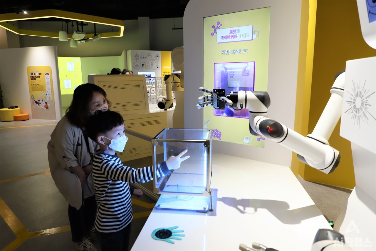 어린이과학관에서 비장한 표정으로 로봇과 가위바위보 대결을 펼치고 있는 어린이 관람객의 모습. (사진=AI타임스).